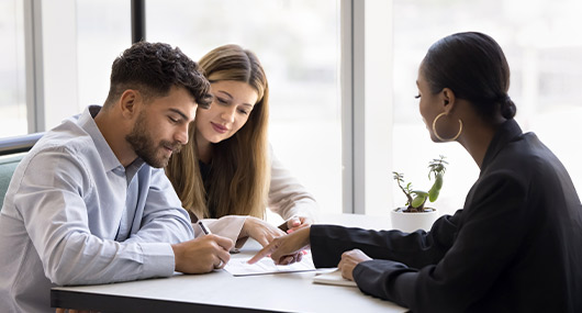 Three people gathered around a table, using a pen and paper to discuss strategies for obtaining a business line of credit.