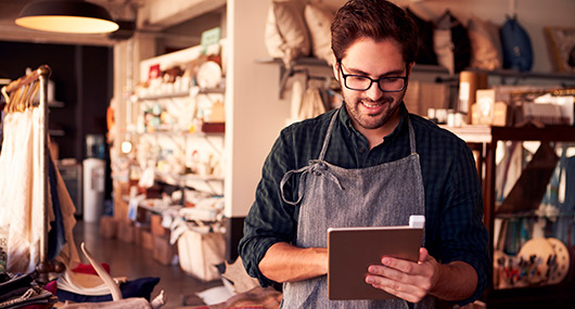 A man wearing an apron is focused on a tablet, likely researching small business loans in Texas.