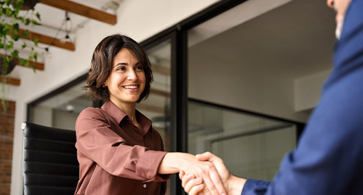 A woman and a man shake hands in an office, symbolizing a successful business partnership or agreement.