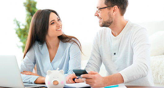 A couple reviews retirement plans, including 401(k)s and IRAs, at a table with a laptop and a piggy bank.