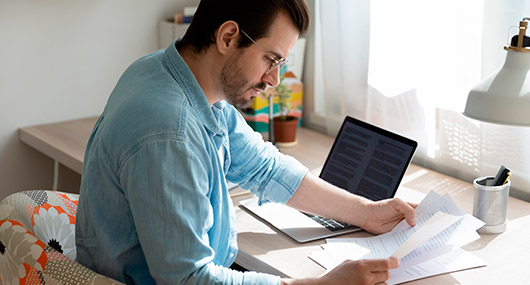 man checking laptop and papers.