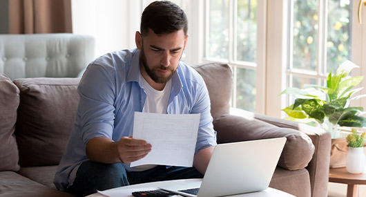 Man sitting on a couch with a laptop and papers, focused on financial planning for Texas residents in the fall.