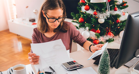 A woman focused on her work at home, with a festive Christmas tree behind her, highlighting holiday budgeting for South Texas families.