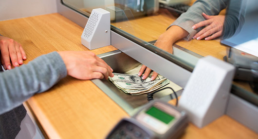 A person depositing cash into a bank machine outside a building, with a focus on the transaction process.